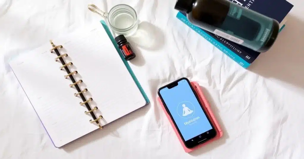 A flat-lay composition of tools for minimalist self-care for moms, including a planner, jar of essential oils, reusable water bottle, meditation app icon on a phone screen, and motivational books arranged neatly on a white linen cloth, emphasizing simplicity and practicality.